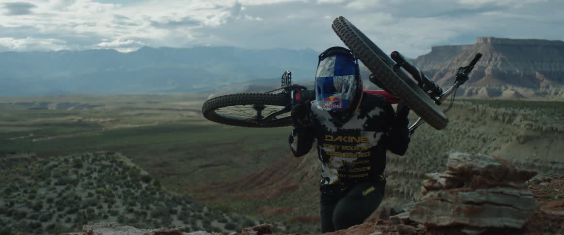 A man carries a mountain bike on his shoulders up a desert slope