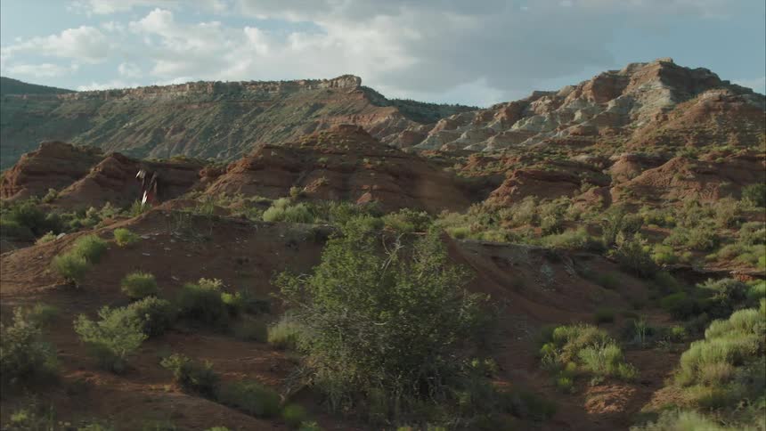 Man riding a mountain bike jumps and does a 360 over a mound surrounded by desert plateaus and canyons
