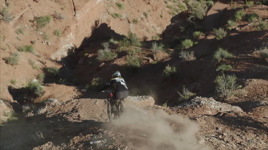 A person riding a mountain bike down a steep and rocky hillside in a desert