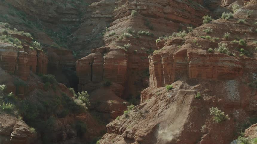 A mountain biker doing a 360 drop while riding off a desert cliff in nature