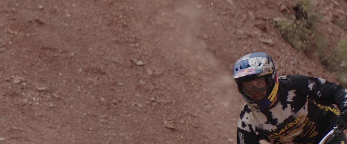 A man with full-face helmet and goggles rides a mountain bike through a dirt corner
