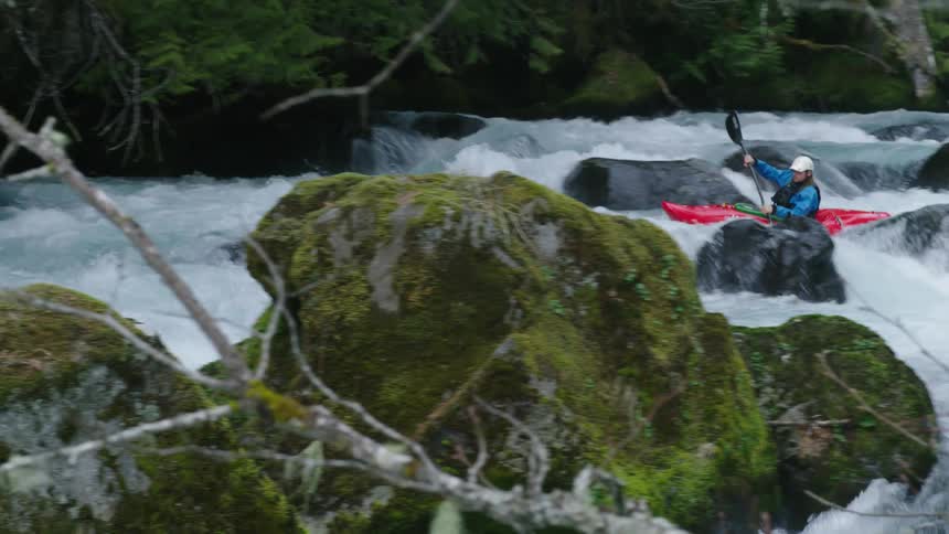 Real time hand held shot of a man in a red whitewater kayak entering a large whitewater rapid paddling around massive boulders