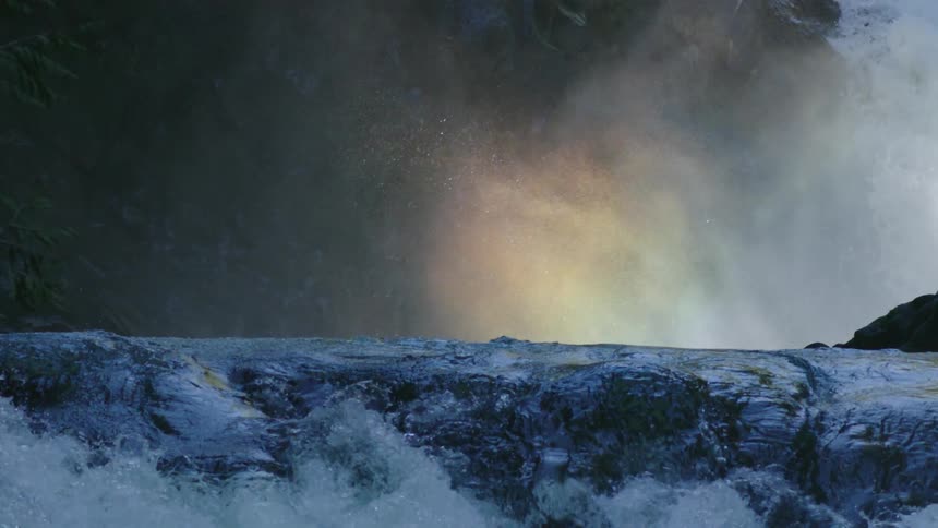 Rainbow forming in the mist at the base of a waterfall on a whitewater river in this magical moment that feels very zen and magical