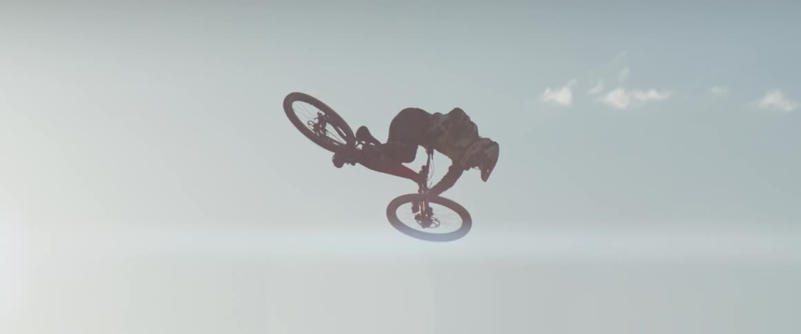 A mountain bike athlete performs a 360 tabletop trick off a desert jump at sunset