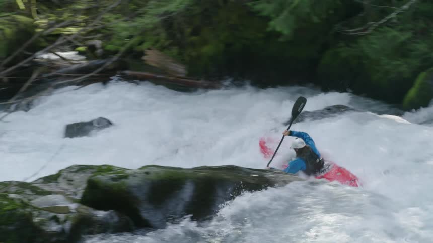Looking downstream in this handheld shot of a man in a red whitewater kayak paddling downstream in a maelstrom of whitewater and intensity