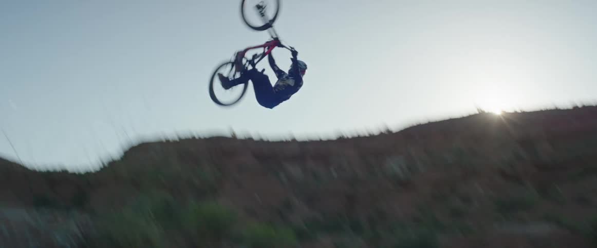 Professional mountain biker hits desert jump and performs a flip trick against the blue sky in the morning