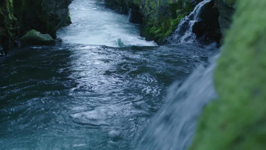 A river and waterfall with a cliff with moss with cascading water exploding into the foreground of the frame