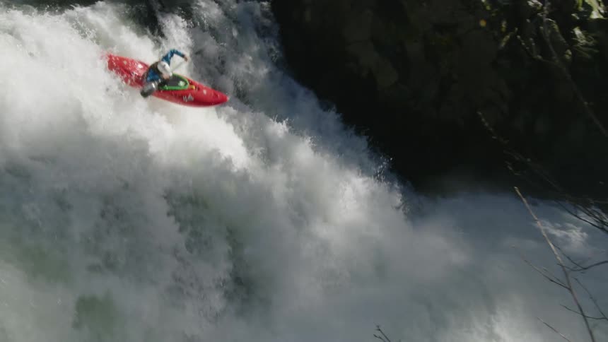 Slow motion shot of a man riding down a large waterfall in dappled afternoon sun with ferns and moss along the river canyon walls