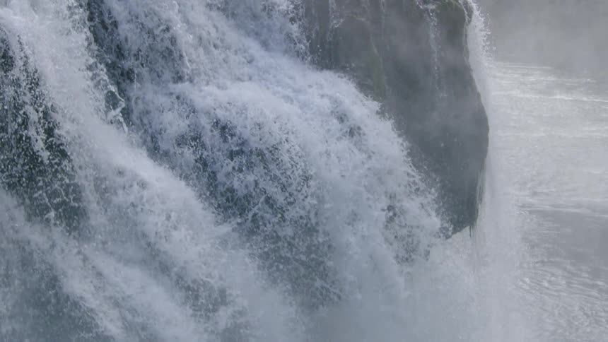 Slow motion shot showing water pouring over the lip of a waterfall and rising in plumes of fine mist from the pool below