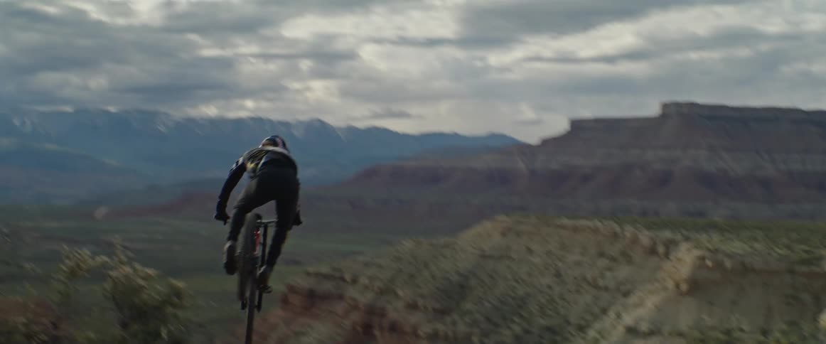 A mountain biker jumping off a cliff and doing a 360 in the air