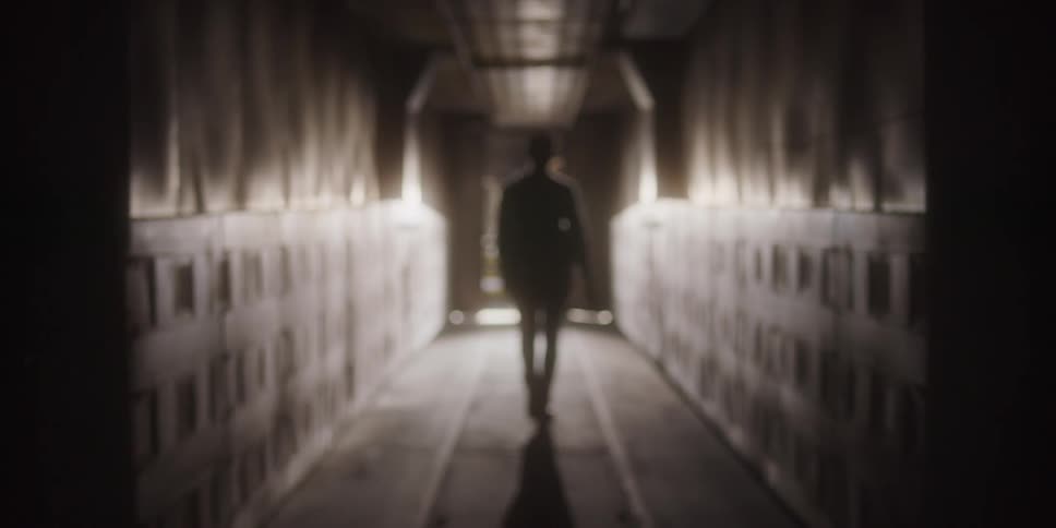Woman wearing a plaid shirt walking down a dimly lit hallway