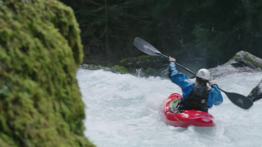 Real time hand held high energy shot of a man in a red whitewater kayak paddling through extreme whitewater on a clean and pristine alpine river
