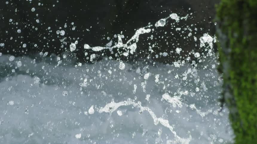 A massive explosion of whitewater covers the frame before disappearing back into the whitewater with a moss covered wall on the right side of the frame