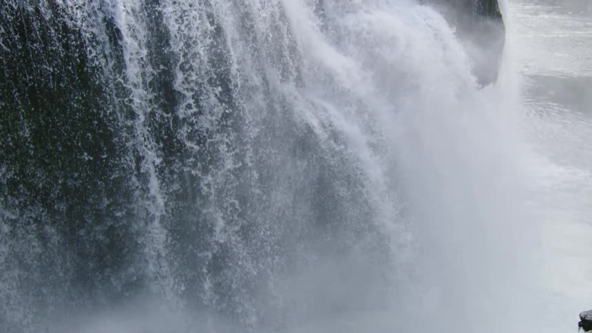 Slow motion shot of water exploding down a cliff face and rising in mist above the pool below deep in the wilderness