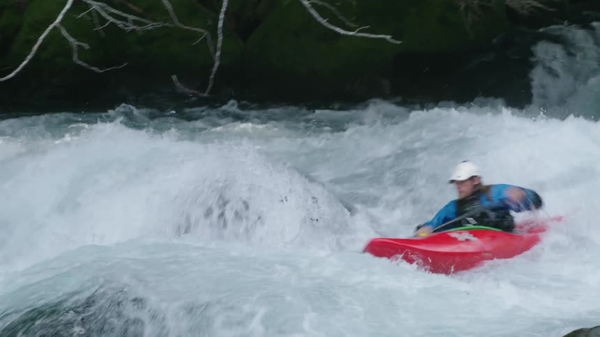 Man in a red whitewater kayak launches down white bubbling and churning whitewater in this high energy shot