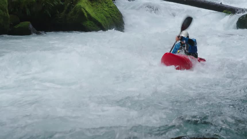 A young man paddles through bubbling and violent whitewater in a red whitewater kayak as he paddles right past the camera in this real-time handheld shot