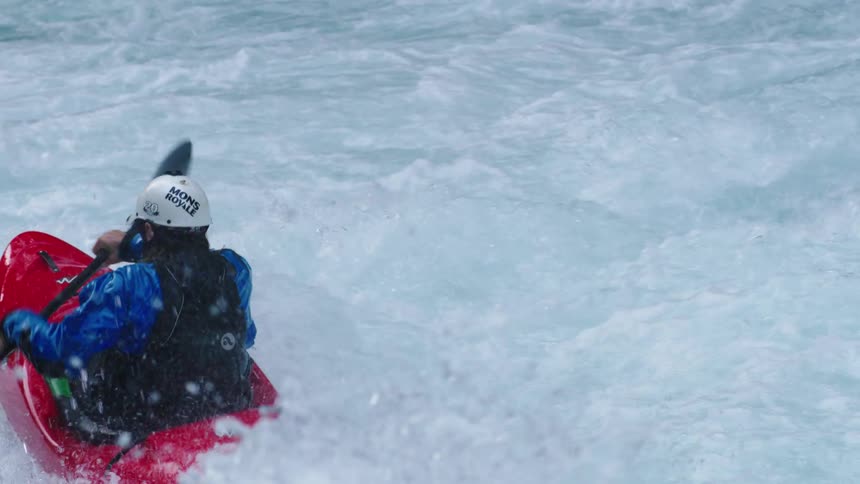 Slow motion shot of a man in a whitewater kayak sprinting downstream in turbulent and boiling whitewater
