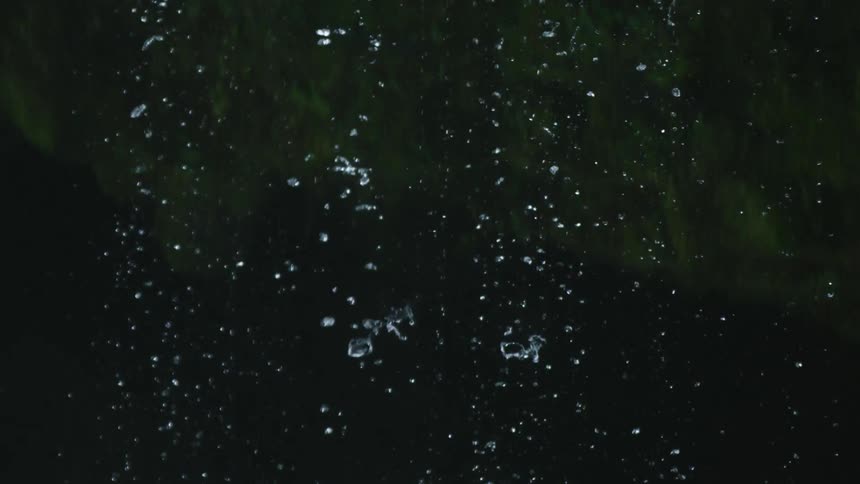 The camera tilts down following droplets as they explode into smaller droplets before crashing on rocks below