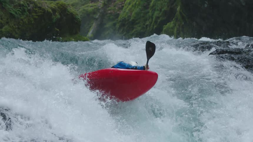 Slow motion shot of a man in a red whitewater kayak launching off the lip of a large waterfall disappearing into the mist at the bottom of a waterfall