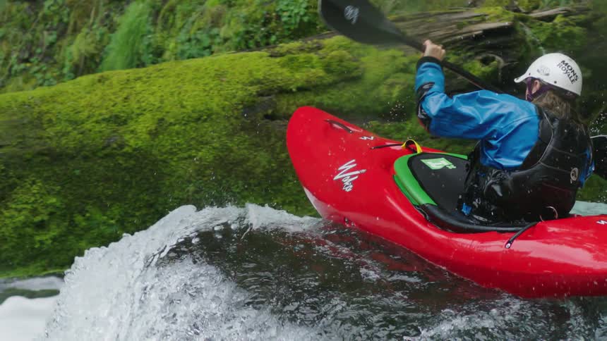 Amazing color contrast of a red whitewater kayak and moss covered green moss in this slow motion shot of a man paddling down a whitewater rapid