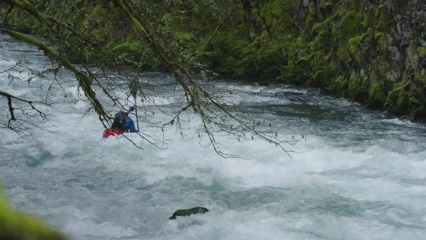Looking downstream as a man in a red kayak whitewater kayaks away from the camera on a clear and clean pristine river with mossy canyon walls