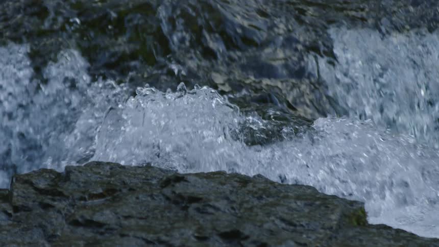 Slow motion shot of water rippling over the edge of the rock and flowing downstream
