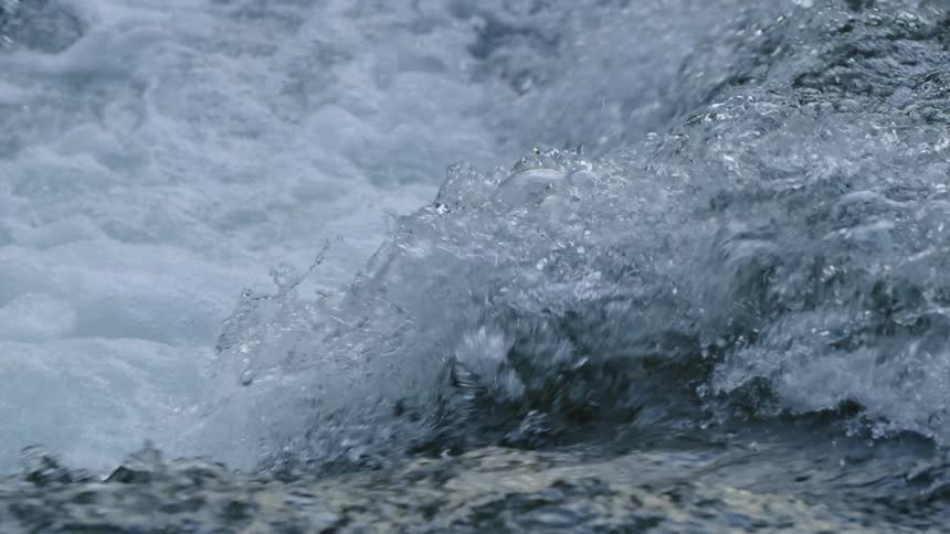 Whitewater explodes upwards as it flows over a fin shaped rock deep in a pristine river canyon in this alpine environment