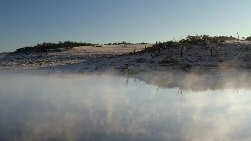 A misty lake surrounded by sandy hills under a clear blue sky