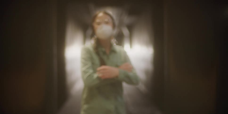 A woman standing in a room in front of walkway with a flare of light crosses her arms and poses for a photo