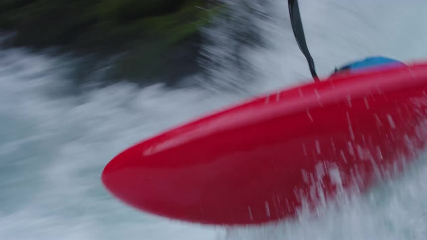 A whitewater kayaker in a red kayak and blue drysuit enters a steep rapid and flies off the lip of the waterfall out of frame