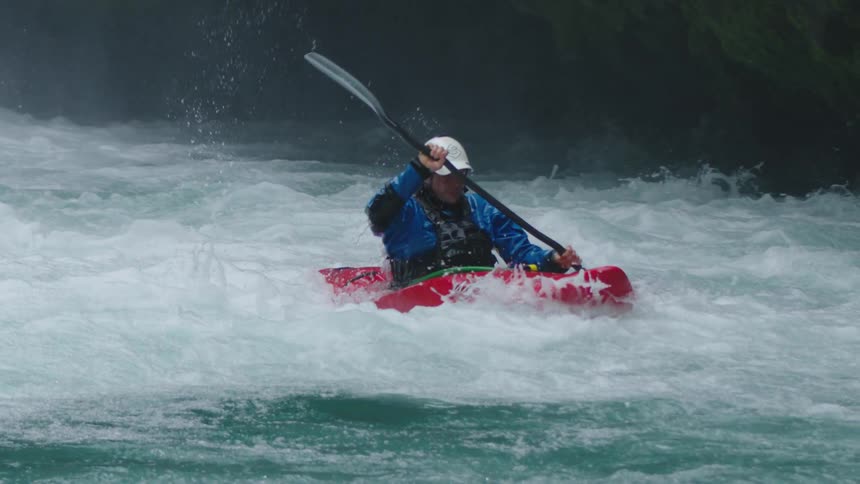 Slow motion shot of a man paddling intensely straight downstream in a red whitewater kayak on a pristine clear river