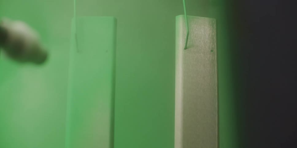 Two pieces of plywood hang from wire as they are painted lime green