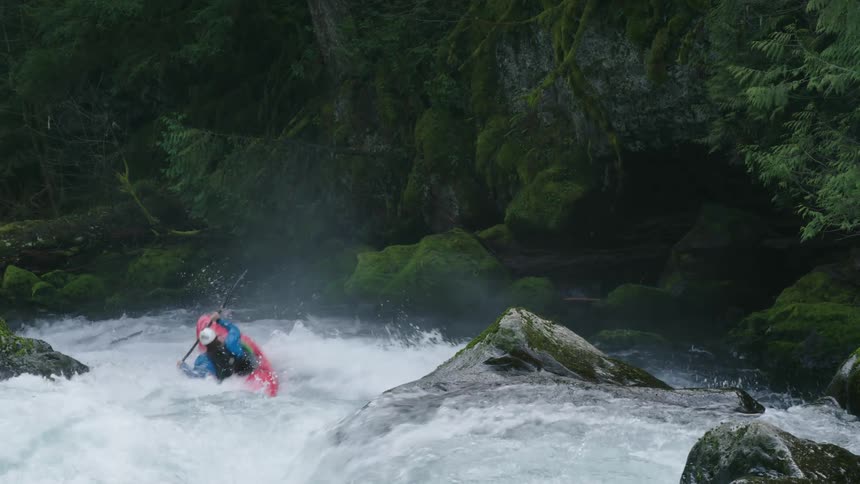 Static shot of a man whitewater kayaking, paddling into a whitewater rapid before disappearing over the lip of a large waterfall