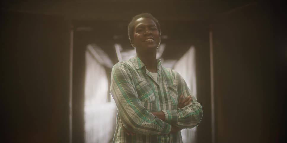 Woman standing in a room wearing a plaid shirt smiles at the camera