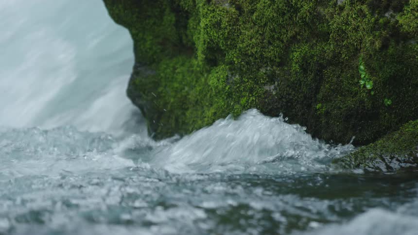 Water rushing around a moss covered rock in this static establishing shot of the Pacific Northwest and clean water