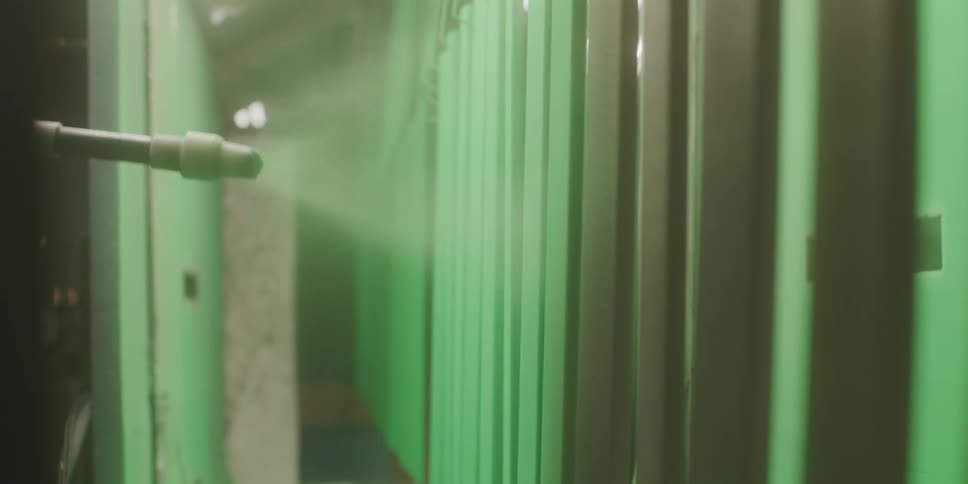 Worker uses a nozzle to spray paint black slabs of plastic in bright green