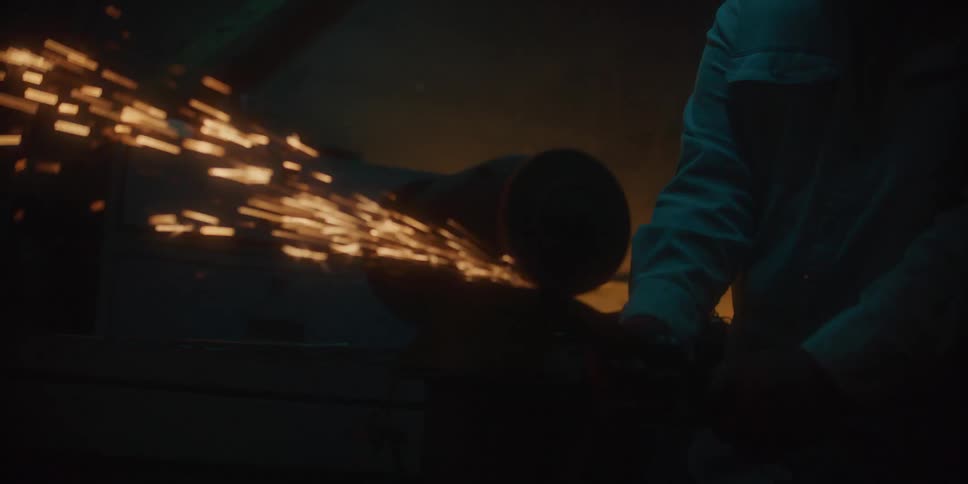 Sparks flying as a person uses a metal grinder inside a dark workshop