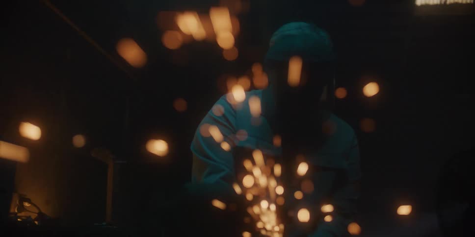 Sparks flying around a man using a power tool in a dark workshop