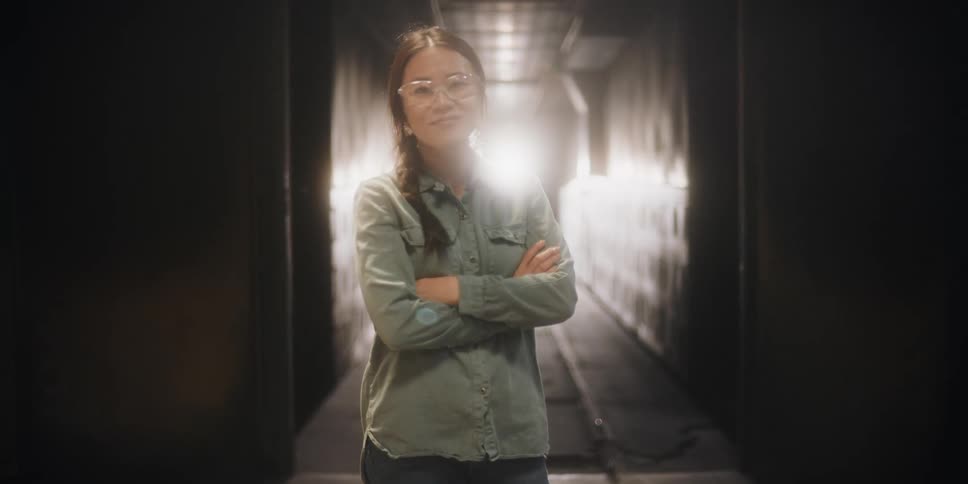 A woman smiles and crosses her arms while standing in a studio in front of a projector showing an image of a hallway