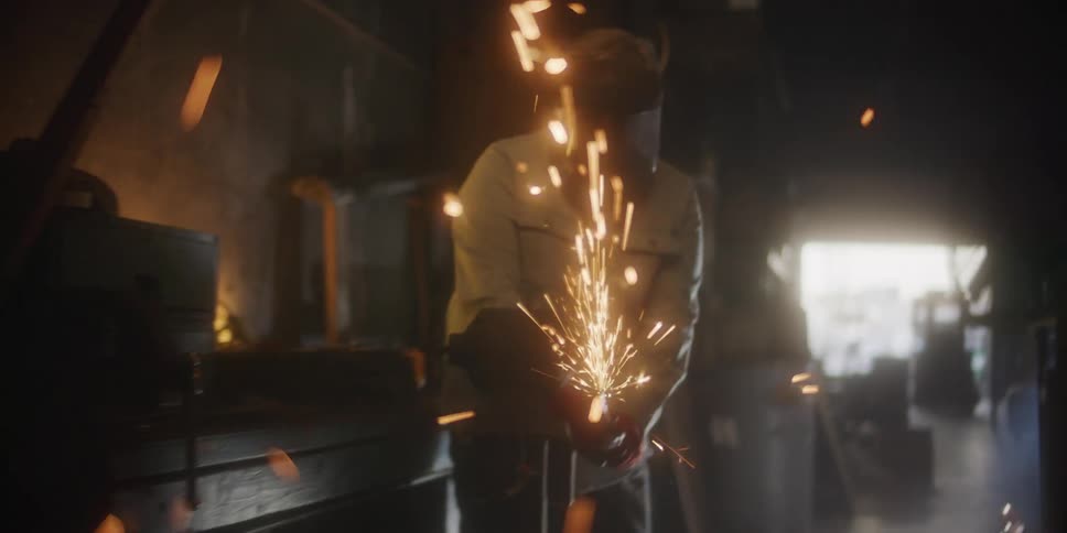 Man working on a dimly lit workshop grinding metal using a power tool