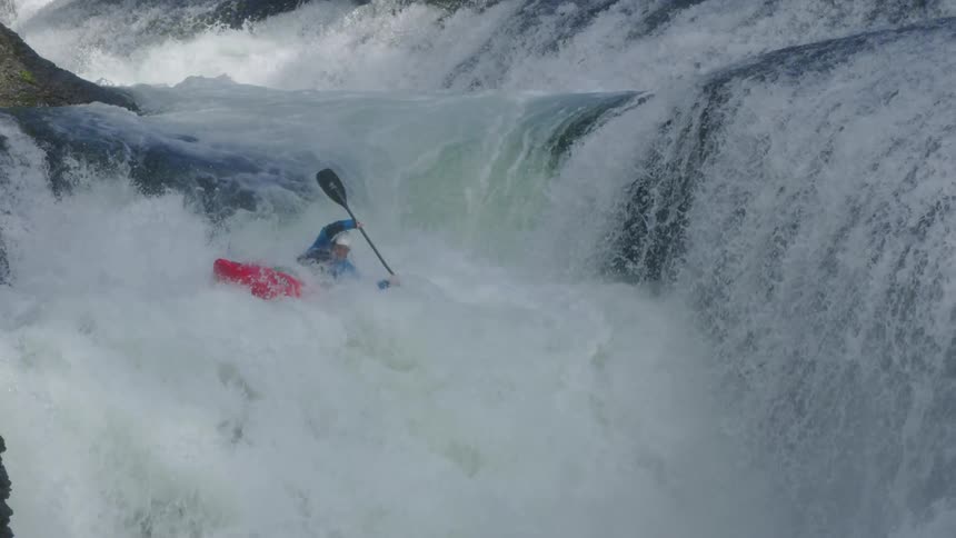 An extremely beautiful double waterfall and a man in a red kayak entering the whitewater and descending both waterfalls before emerging at the bottom of the rapid