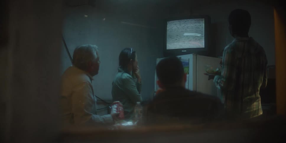 Coworkers in break room eat while watching signal snow on television sitting on refrigerator
