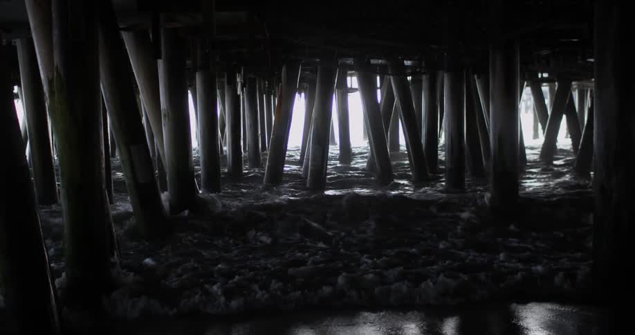 Waves crash on the posts under a pier