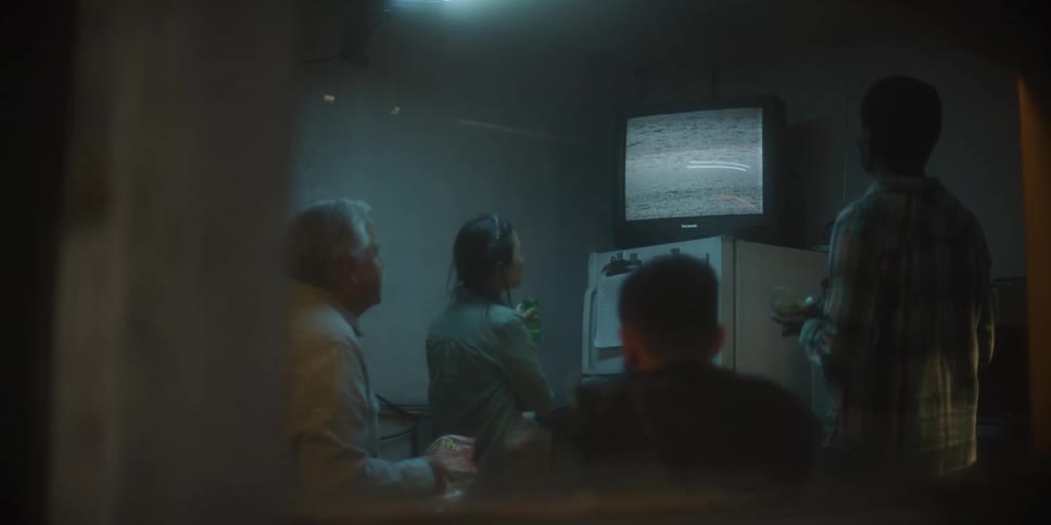 Group of people sitting in a dimly lit room looking at the static on a vintage television screen