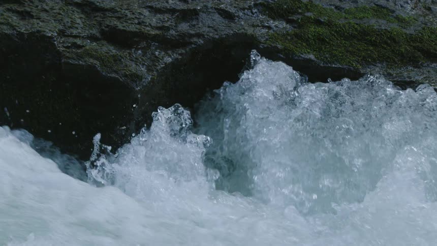 Tight establishing shot of water boiling up against a cliff edge and boiling up into the air