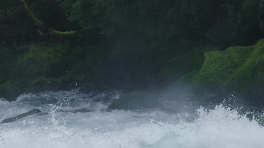 Fast moving river water splashes up and onto the side of a moss covered canyon in this slow motion shot of light and dark