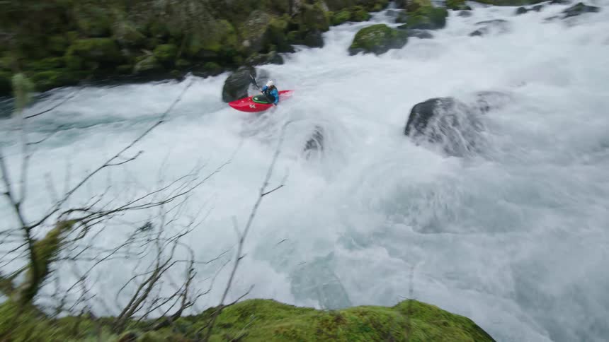 Super wide rapid pan from right to left as a man in a red whitewater kayak navigates a raging whitewater river in his creekboat