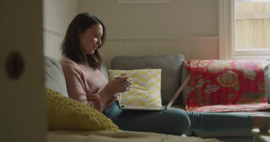 A white woman sits on a couch and looks at a laptop