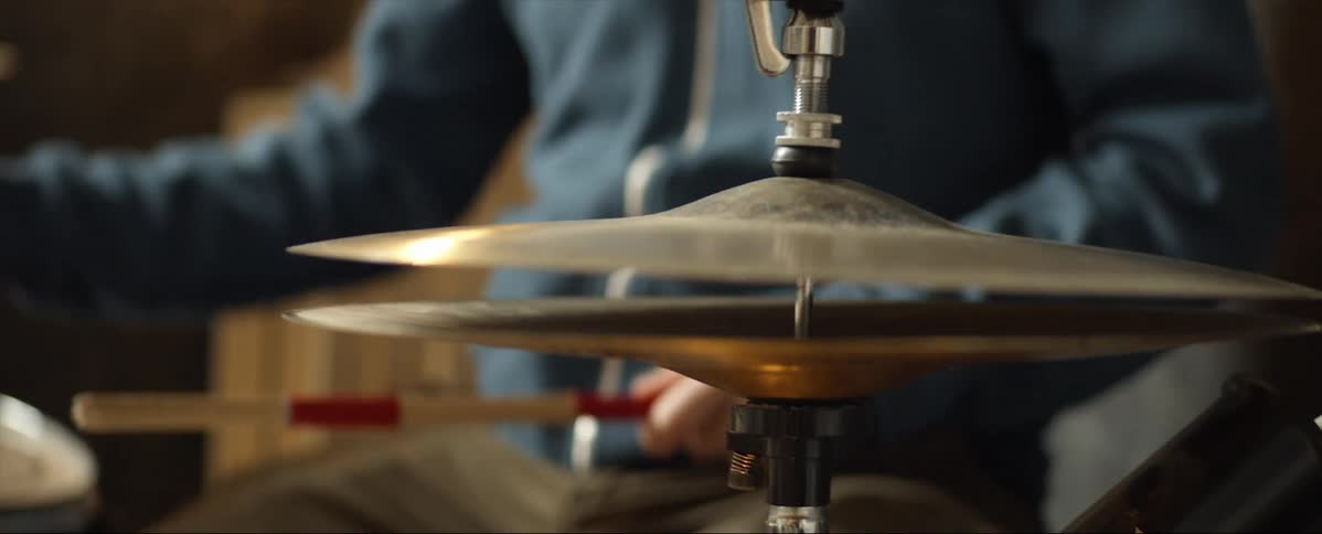 A man sits in front of a drum set and hits it with sticks
