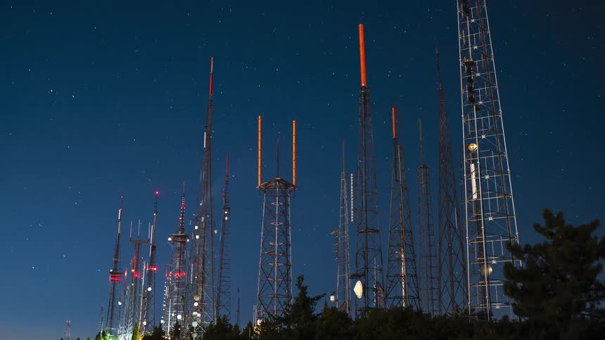 Timelapse of communication towers over a mountain lighting up at night